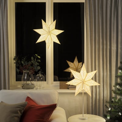 Cosy living room with warm STRÅLA star lamps, red cushions, and a lit christmas tree.