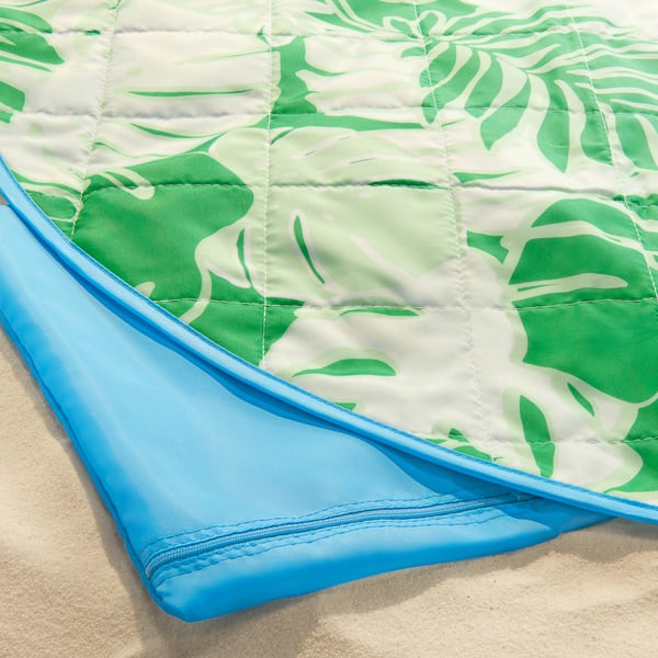 Folded tropical leaf-patterned picnic blanket with blue edges. Soft, quilted texture. Beach or park essential.