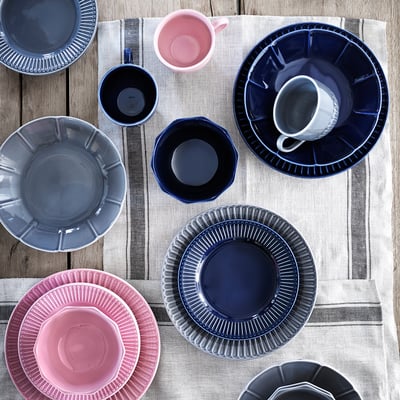 Blue, pink, grey STRIMMIG dinnerware with floral designs on striped tablecloth.