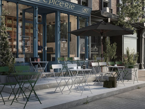 Outdoor cafe with blue-framed windows and folding green chairs; tables with black umbrellas line the pavement.