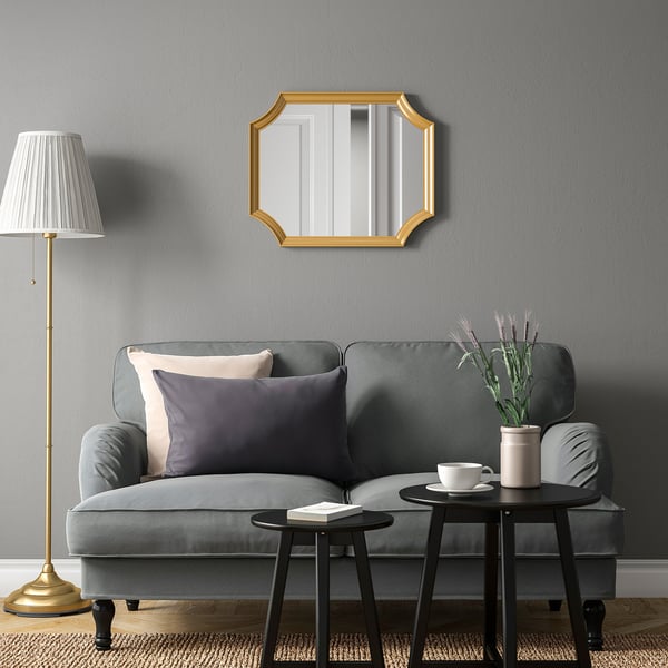 Modern living room with grey sofa, gold mirror, black tables, and tall lamp.