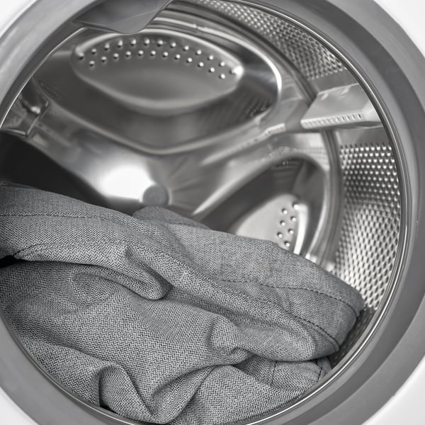 Washing machines drum with wet grey sweater clothes.