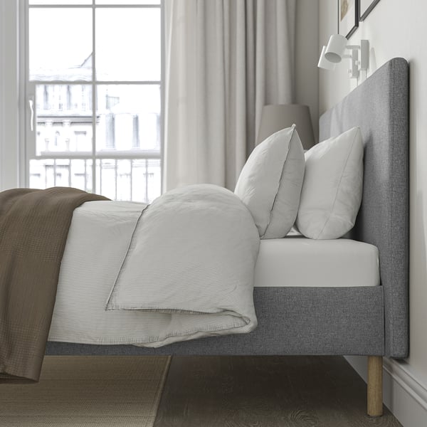 A minimalist bed by a window, with a grey headboard and white pillows, showcasing a clean, modern design.