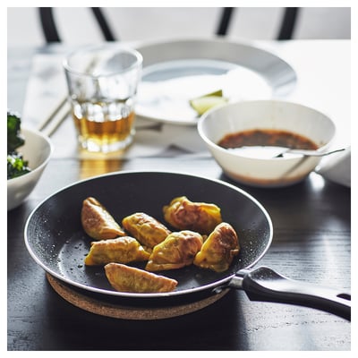 Black frying pan with golden dumplings, accompanied by dipping sauce, lime, glass of drink, and utensils.