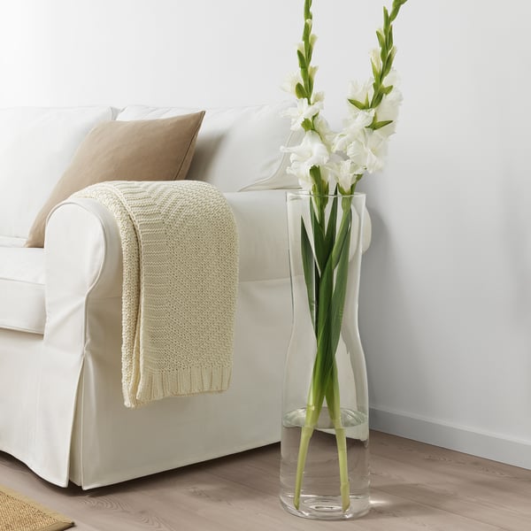 Glass TIDVATTEN vase with flowers by sofa.