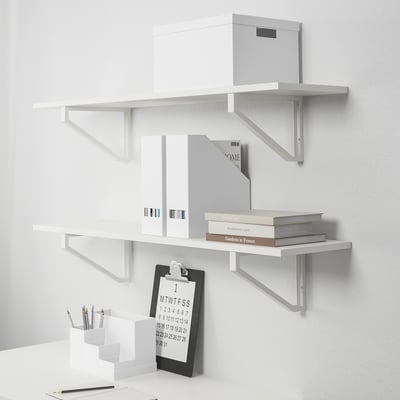 White wall shelves with books, boxes, and a clipboard with pens. Organised home office storage setup.
