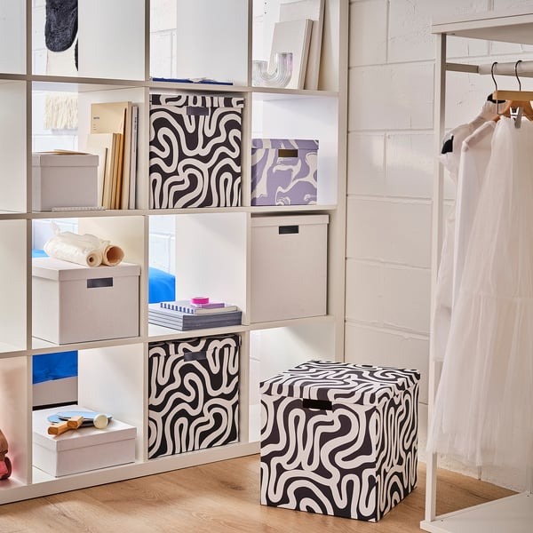 A TJENA box with a black and white patterned design on a shelf in a room. The box is square-shaped and made of sturdy recycled paperboard.