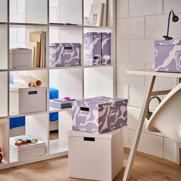 Storage shelf with purple-patterned TJENA boxes, made of recycled paperboard, holding various items.