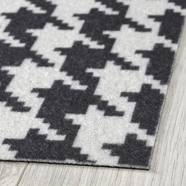 Abstract black and white geometric door mat on wooden floor, showcasing quality design and material.