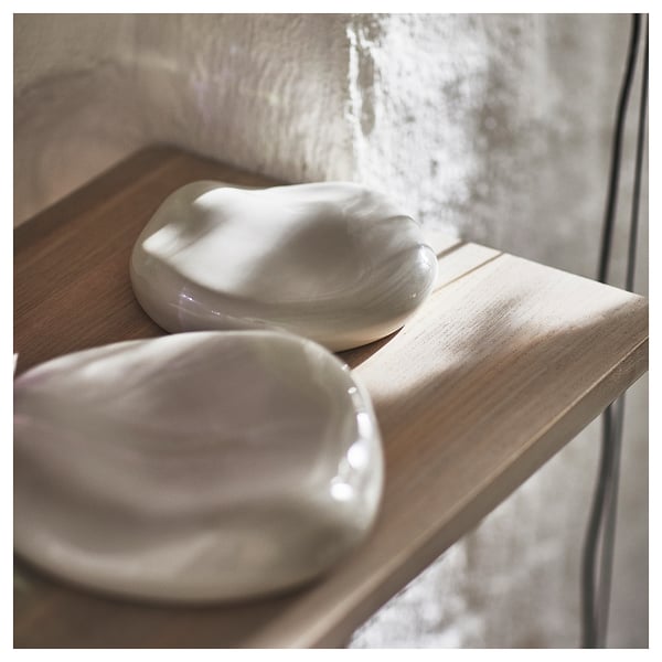Two white, ceramic wall decorations of organic shapes sit on wooden shelves, evoking a natural, earthy aesthetic.