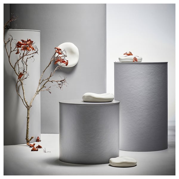 Three grey vases with unique white ceramic shapes. One holds a dried branch with flowers against a grey wall.