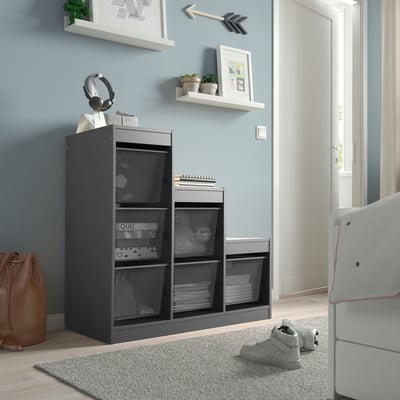 Modern black TROFAST storage unit with mesh baskets. Wall shelves with plants and art. Blue wall, nearby door.