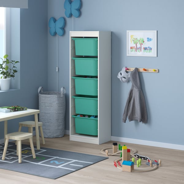 Childs room with TROFAST white/teal storage. Tall, narrow wood & teal plastic bins. Grey hoodie, toys, blue decor, picture frame.