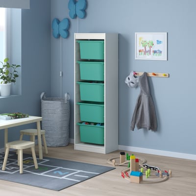 Kids playroom with TROFAST storage, blue butterflies, green boxes, grey hoodie, small table, chairs, toy train, and striped laundry basket.