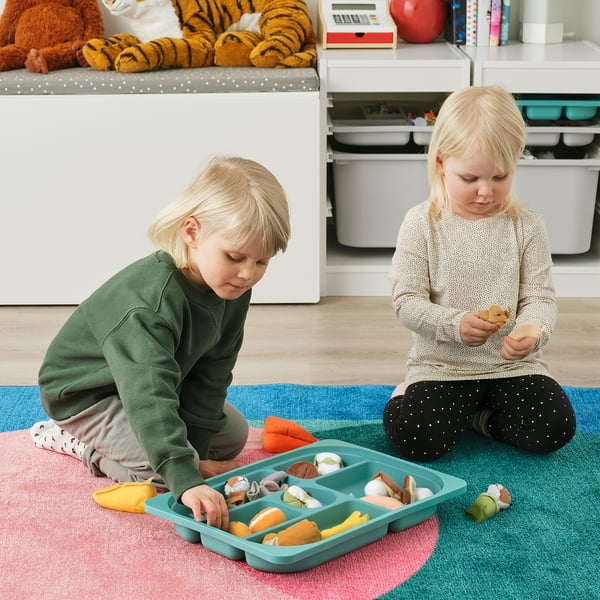 Two children playing with colourful toys on a multicoloured rug next to a storage tray with compartments.