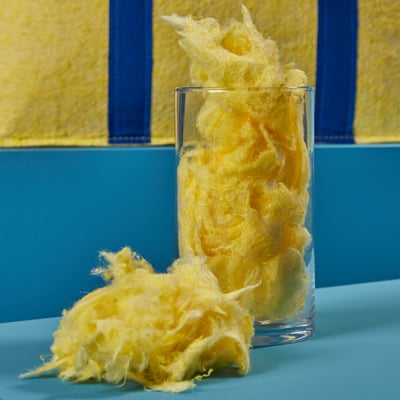 Yellow candy floss in glass; soft, fluffy, oversized dessert.