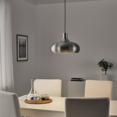 Modern dining area with VÄXJÖ hanging lamp, sleek metal design, subtle glowing shade, surrounded by chairs, table, and decor.