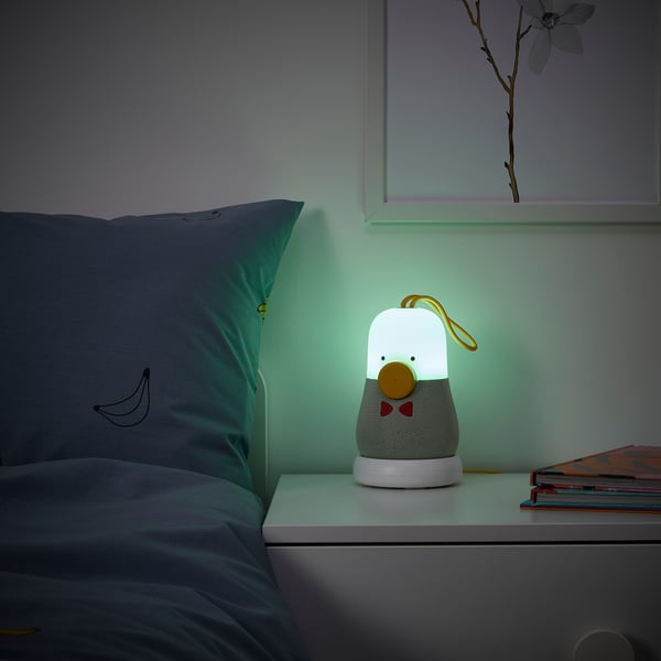 A bedside table with a childs lamp playing music and emitting a soft green light.
