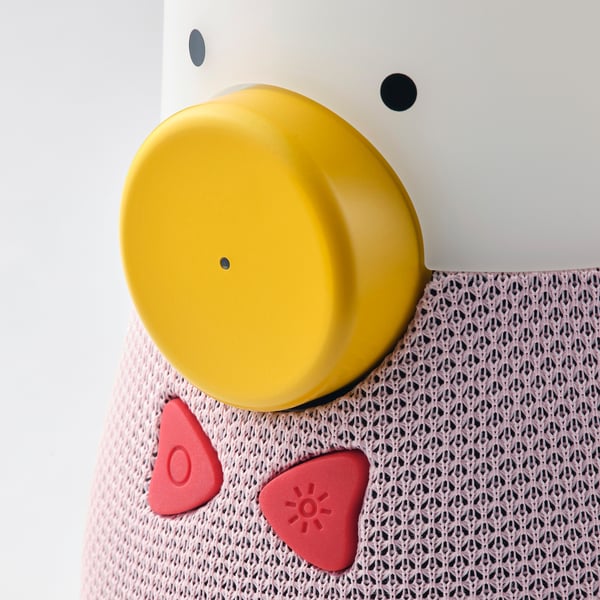 This image shows a kid-friendly speaker with a yellow top and red controls. It sits on a pink mesh surface.