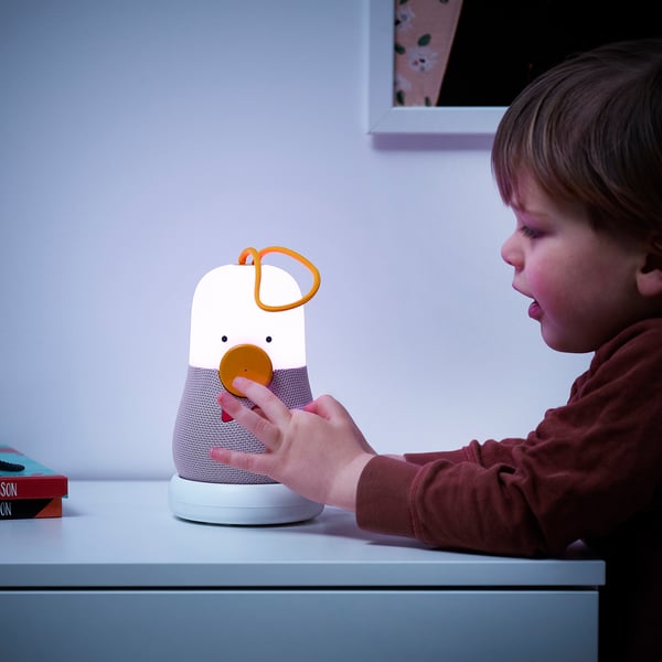 A child interacts with a VAPPEBY speaker lamp, adjusting its dial while the light illuminates, showcasing its fun and functional design.