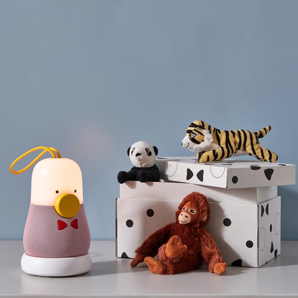 Three plush toys sit atop stacked decorated storage boxes, with a yellow loops and red bow device beside them.
