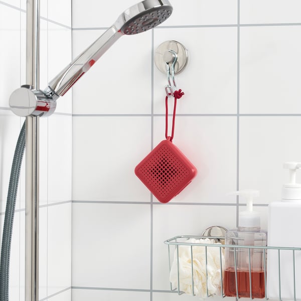 A red portable bluetooth speaker hangs near a shower, playing music in the bathroom. Its waterproof and suitable for wet areas.