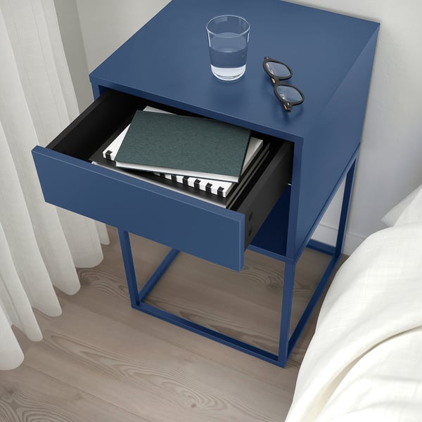 Blue bedside table with drawer open showing books, glasses, and a glass of water on top.