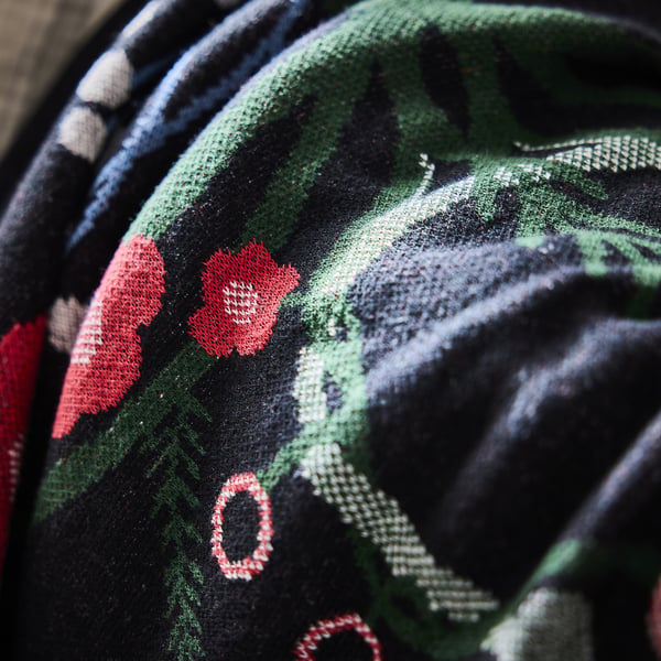 Close-up of a soft, textured throw blanket featuring a green and black plaid pattern with red floral accents, draped over a piece of furniture.