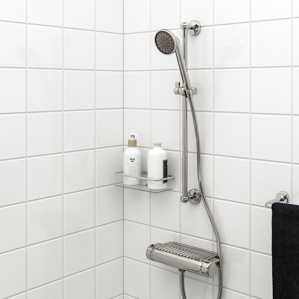 Modern shower setup with VOXNAN chrome rail and full spray handshower, holding bottles and towel on white tiled wall.