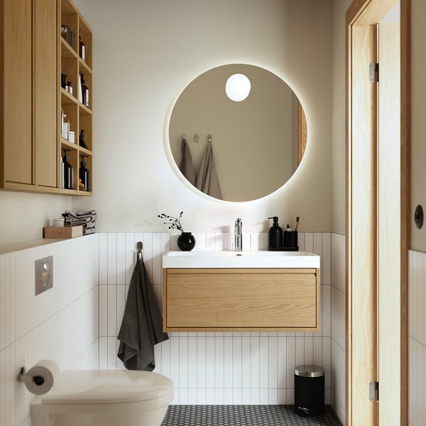 Modern bathroom with oak vanity, single drawer, white counter, lit mirror, minimalist design.