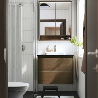 Modern bathroom with oak ÄNGSJÖN vanity, drawers, white sink, wall-mounted, mirror, plant, black stool, chrome tap.