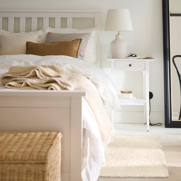 Cosy bedroom with white rug, basket, bedside lamp, and large cream blanket on bed.
