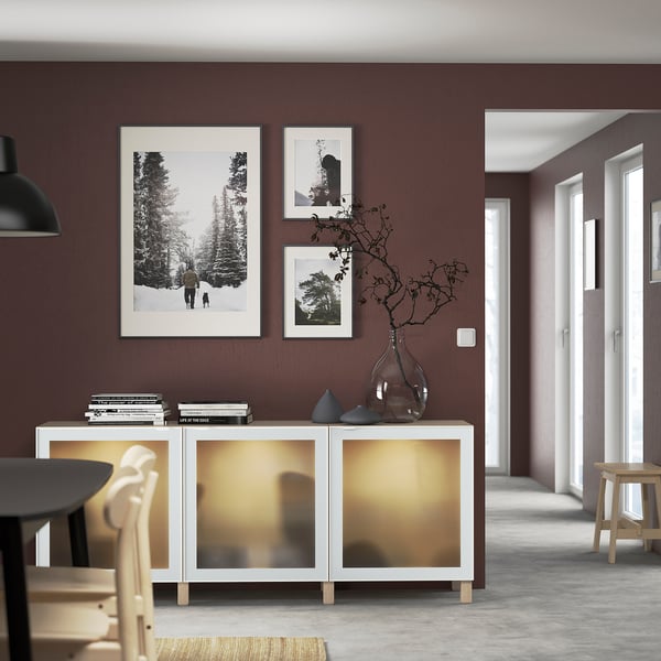 White BESTÅ sideboard with glass door and open shelves against dark wall.
