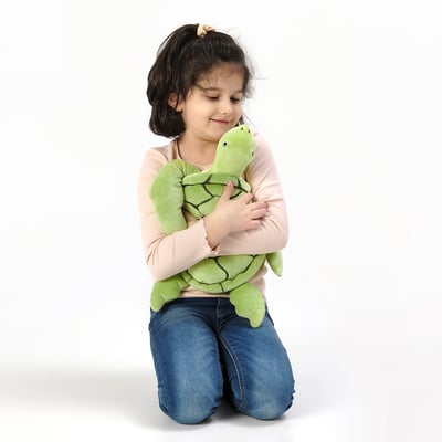 A young girl hugs a green turtle cuddly toy; both kneel, showing comfort and safety.