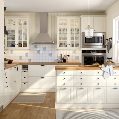 Modern off-white kitchen with glass cabinets, blue tile backsplash, stainless steel appliances, wooden countertops, and pendant lighting.
