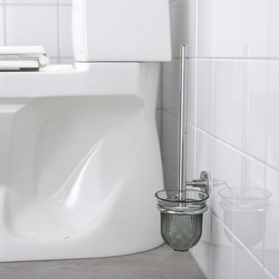 A chrome-plated toilet brush holder mounted on a white tiled bathroom wall, concealing fixings and keeping the brush handy and off the floor.