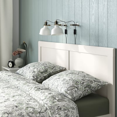Bed with dual wall lamps, paisley bedding, bedside table with alarm clock.
