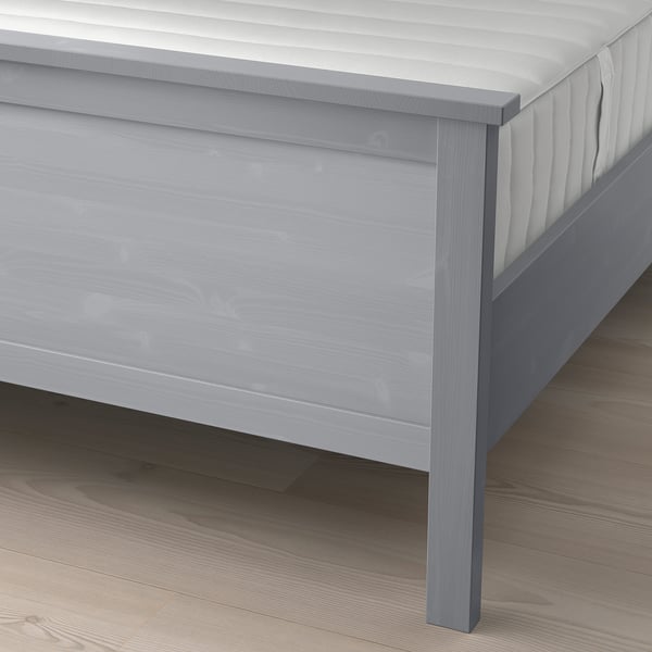 Light wooden bed frame with grey finish, sturdy legs, and adjustable bed sides to fit various mattress thicknesses, positioned on a wooden floor.