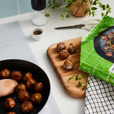 Cooked vegetables displayed on a wooden cutting board and a black plate, with a green-packaged vegetarian meal on the side.