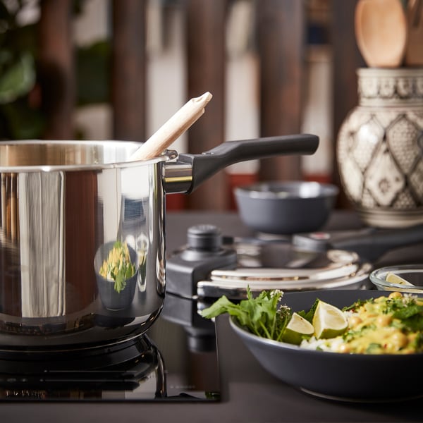 Modern kitchen setup with stainless steel IKEA 365+ pressure cooker on black stovetop, alongside colourful bowl of food.