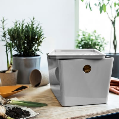 Grey KUGGIS box with handle, surrounded by plants & tools. Medium size, made from recycled plastic.