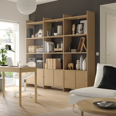 A light wooden LÅDMAKARE storage system against a dark wall. It open shelves and cabinet doors, displaying decor items and books.