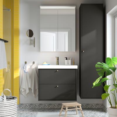 Modern bathroom with black vanity, mirror cabinet, yellow-tiled shower, white sink, grey towels, plant, and small stool.