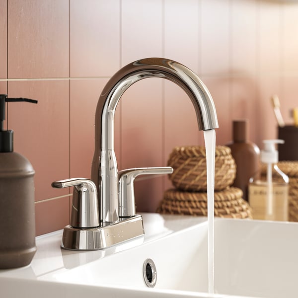 Modern chrome sink tap with curved design runs water, set against pinkish wall.
