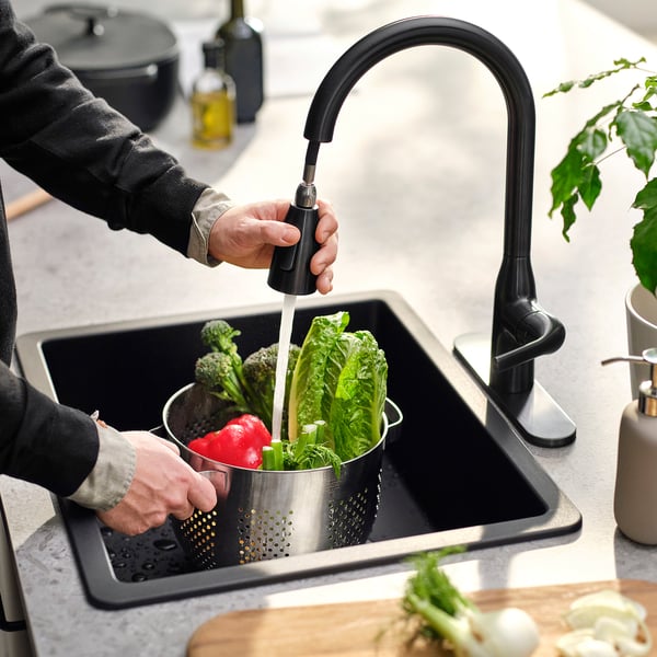 Person washes vegetables in sink using pull-down spray from black kitchen tap.