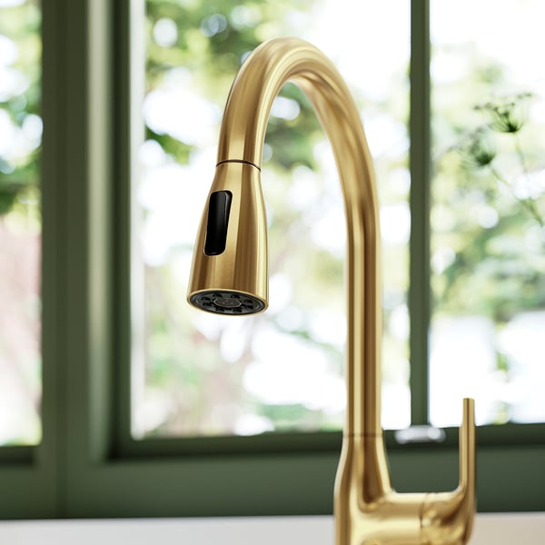 Gold kitchen tap with a sleek gooseneck design and pull-down spray head, positioned near a window.