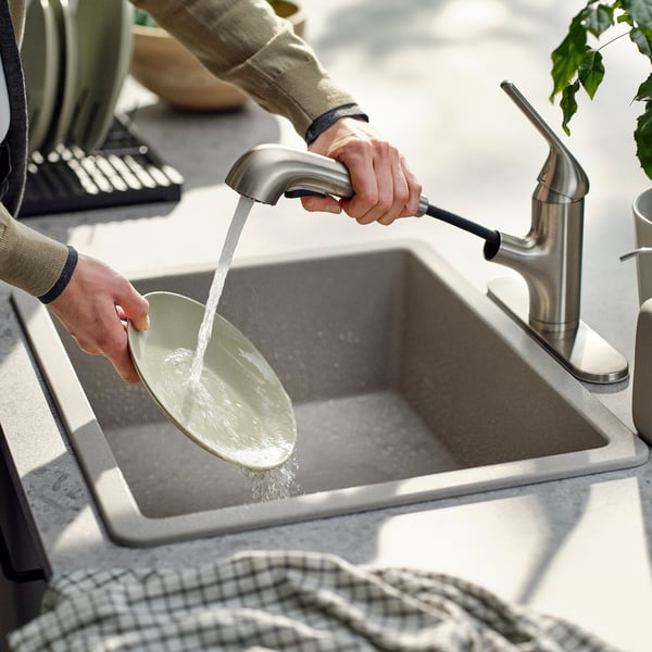 Person washing plate under modern kitchen tap with pull-out spray head.