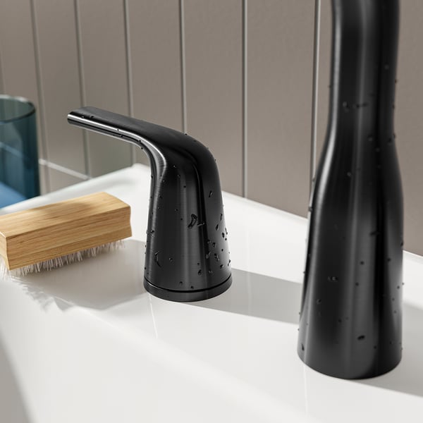 Black modern sink tap with sleek curves, matte finish, and water droplets, adjacent to a wooden brush.