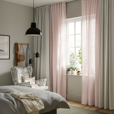 Bedroom with MATILDA sheer pink curtains, striped & bubbly, beside a large bed with patterned pillows, wall lamp, and nearby plants.