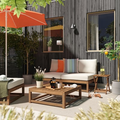 Modern patio with grey NÄMMARÖ sectional, coffee table, orange umbrella, black house, large windows.